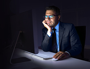 Kaufmann sitzt in dunklem Büro an seinem Schreibtisch vor dem PC
