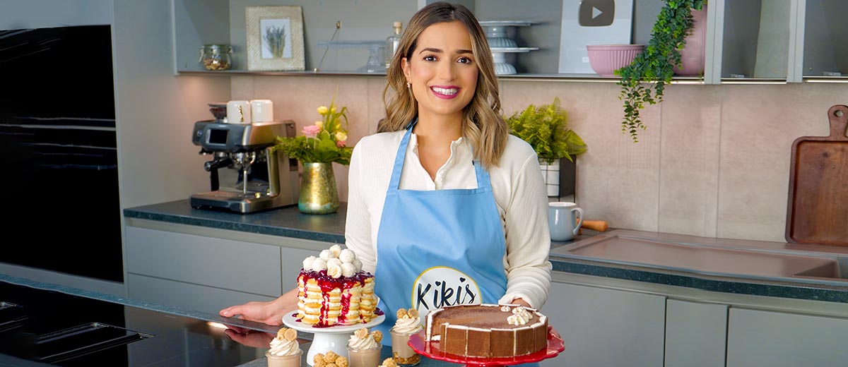 Abbildung: Youtuberin und Backexpertin Kiki in der Küche mit versch. süßen Leckereien wie eine Torte und ein Kuchen