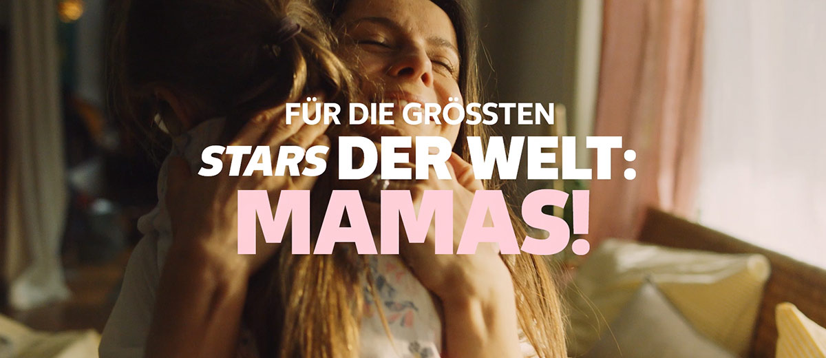 Tochter umarmt ihre Mutter; Schriftzug: FÜR DIE GRÖSSTEN STARS DER WELT: MAMAS!