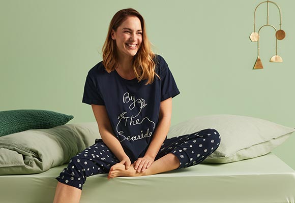 Abbildung: Frau in Pyjama sitzt auf einem Bett mit grüner Bettwäsche