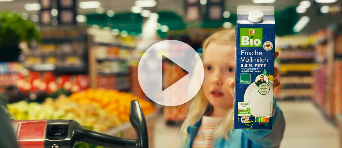 Ein Mädchen steht in einer Kaufland-Filiale und hält eine K-BIO Bioland Frische Vollmilch in der Hand; Abbildung: Play-Button
