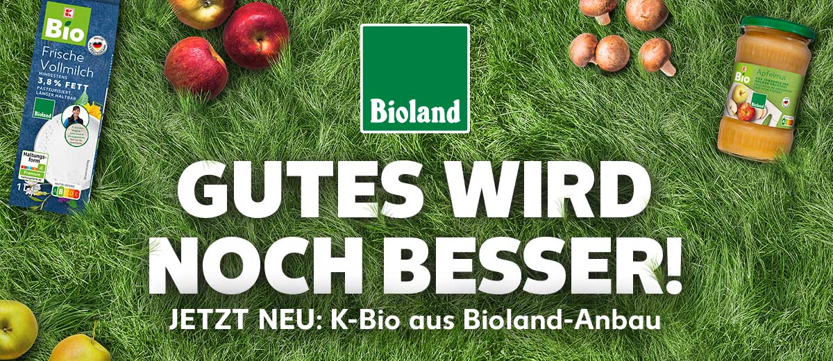 Logo: Bioland; Schriftzug: GUTES WIRD NOCH BESSER! JETZT NEU: K-Bio aus Bioland-Anbau; Hintergrund: Grüner Rasen mit Äpfeln und Pilzen; Produktabbildungen: K-BIO Bioland Frische Vollmilch, K-BIO Bioland Apfelmus