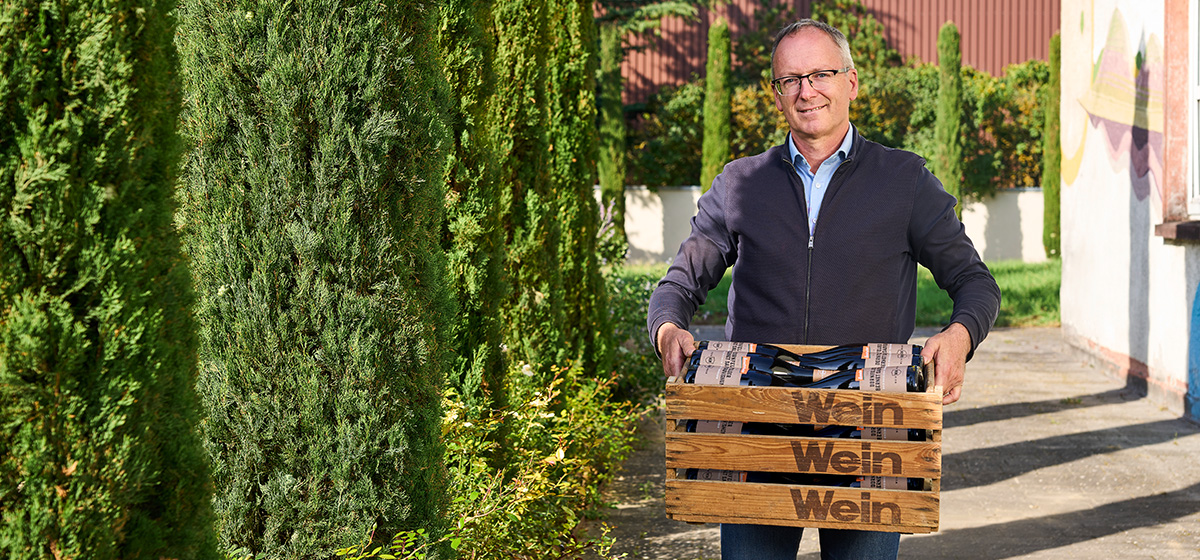 Abbildung: Winzer Hubertus Weinmann trägt eine Kiste mit Weinflaschen