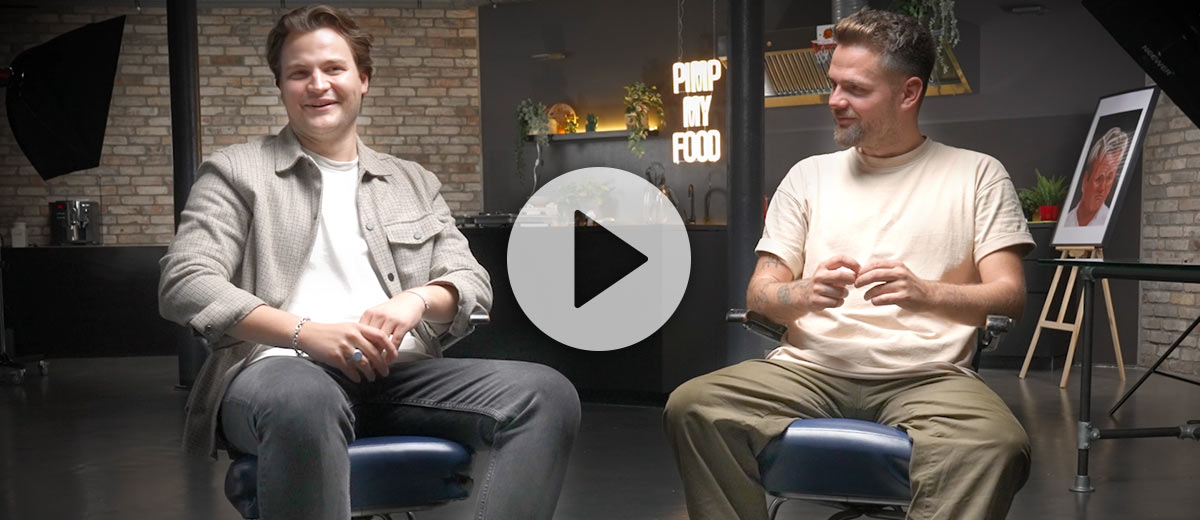 Abbildung: Foodie Niklas und Koch Andy sitzen in der Pimp my Food Küche; Abbildung: Play-Button