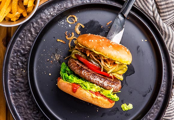 Abbildung: Burger von oben auf einem schwarzen Teller fotografiert, daneben eine kleine Schale mit Pommes