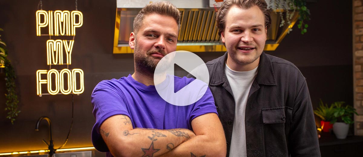 Abbildung: Foodie Niklas und Koch Andy stehen in der Pimp my Food Küche; Abbildung: Play-Button