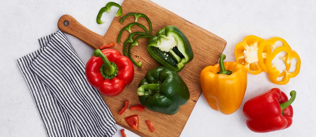 Abbildung: Rote, grüne und gelbe Paprika auf einem Holzbrett