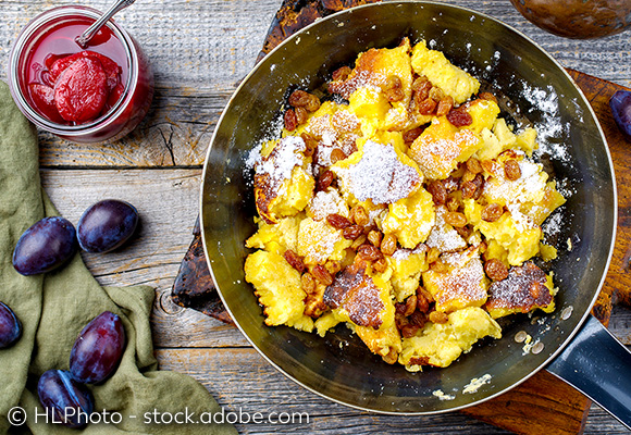 Abbildung: Kaiserschmarren in einer Pfanne. Daneben eingelegte Zwetschgen in einem Glas; © HLPhoto - stock.adobe.com
