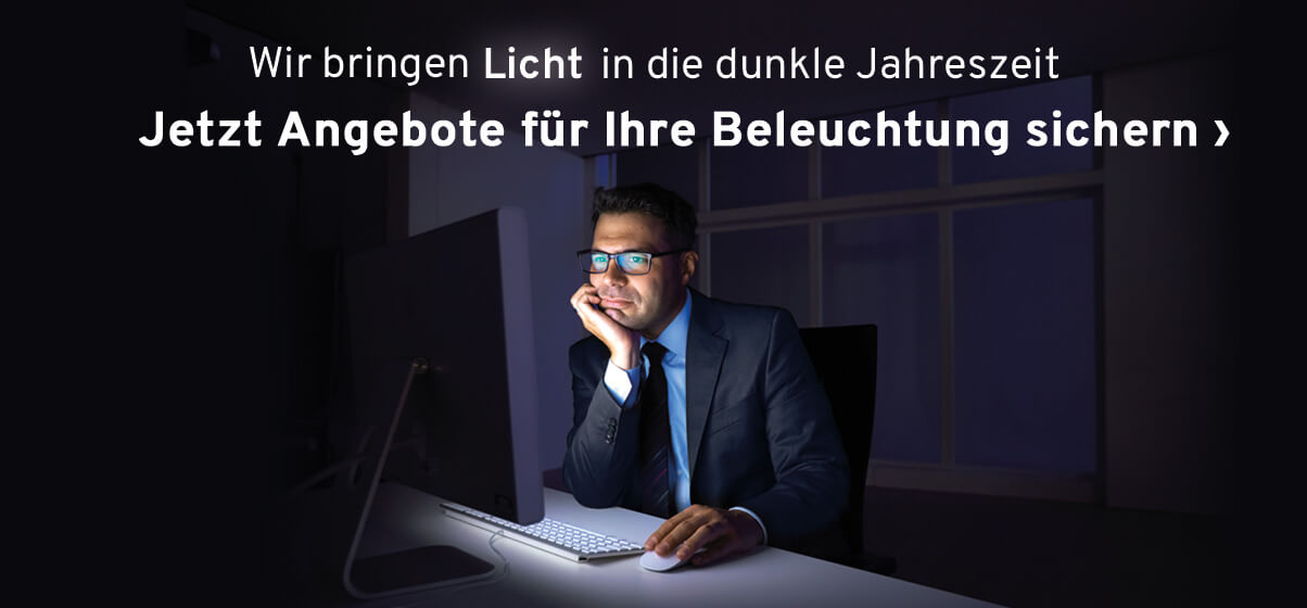 Mann sitzt am Schreibtisch im dunklen Büro, ohne Schreibtischlampe