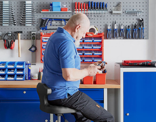 Handwerker an Werkbank mit Schraubenzieher in der Hand und Handwerkzeug an der Wand