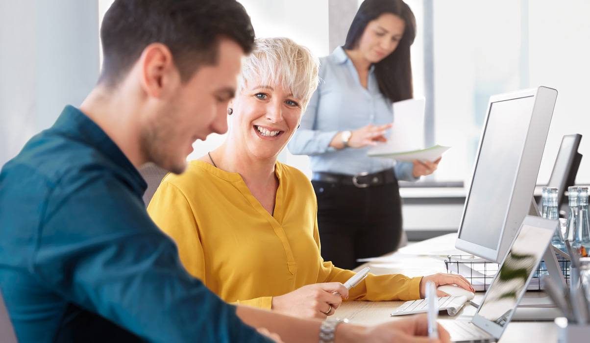 Drei Personen mit freundlichem Gesicht am Schreibtisch